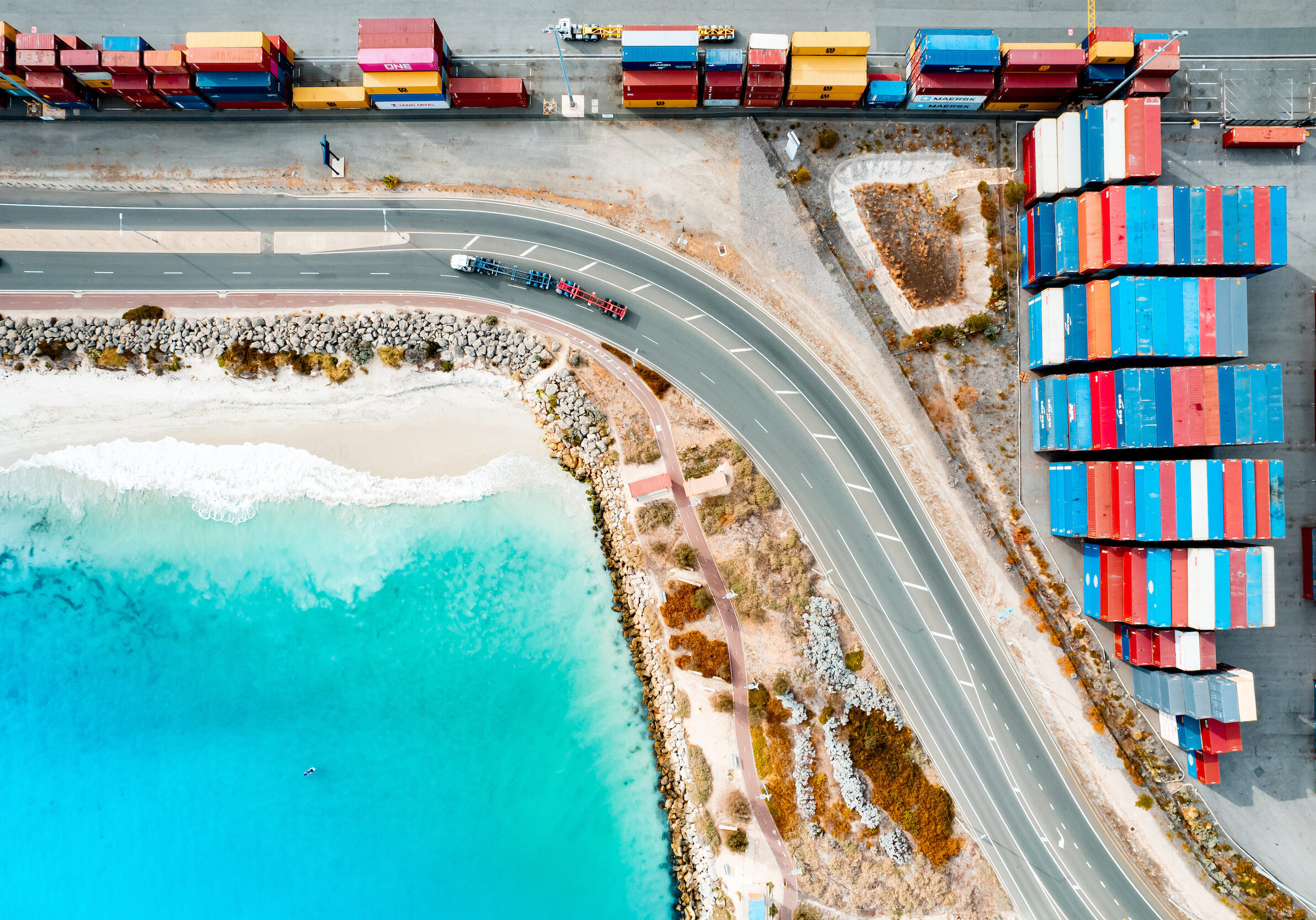 Shipping containers at Fremantle Port with white sandy beach and crystal clear blue sea